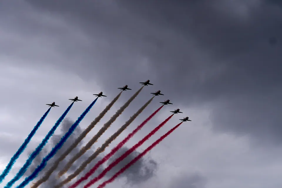 The Red Arrows climb through a grey sky, trailing parallel red, white and blue smoke