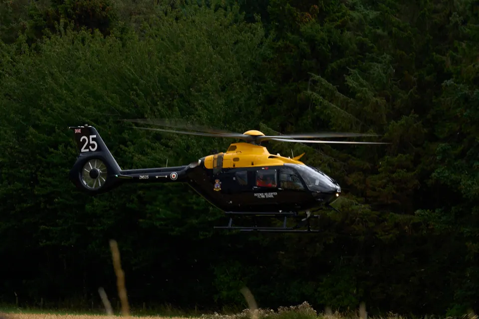 A yellow and dark green helicopter flies low against a forested hillside