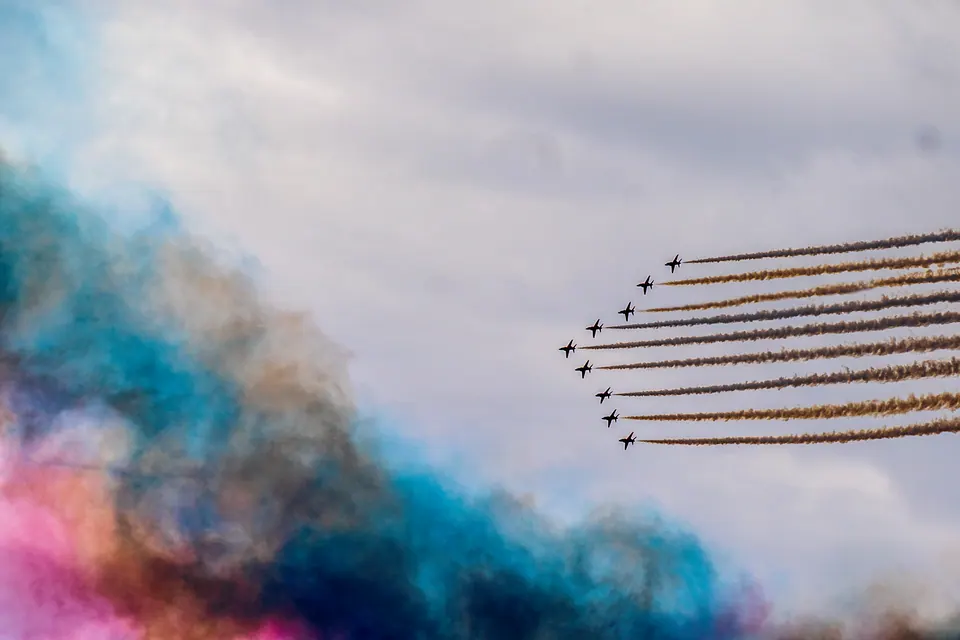Aircraft sweep in from the right above clouds of blue, white and red smoke