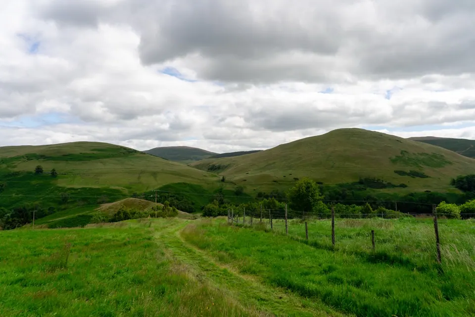 A grassy track runs between rolling hills under heavy grey clouds