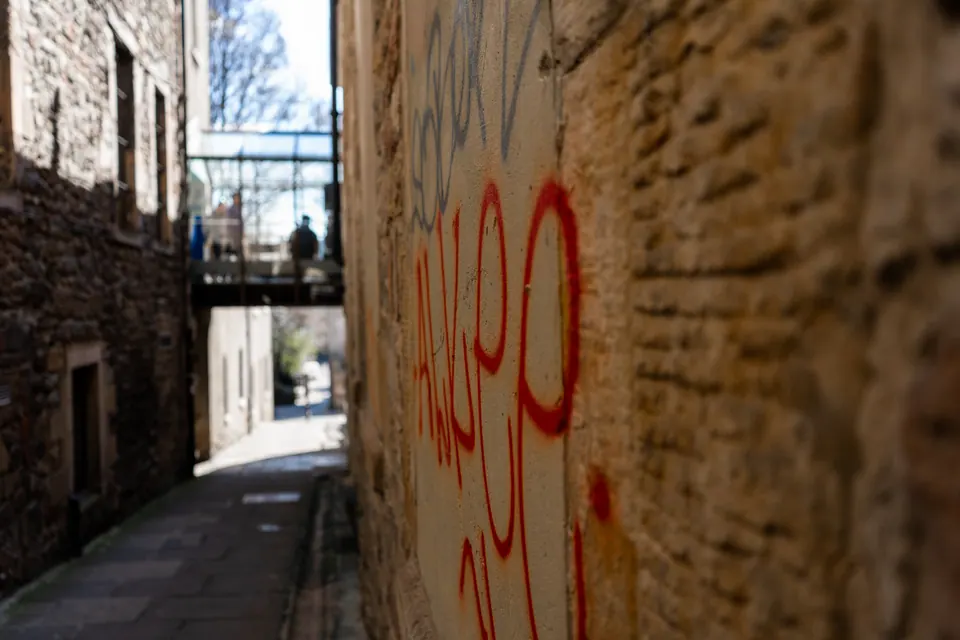 Red graffiti on a sandstone wall beside a narrow Edinburgh passage and overhead walkway.