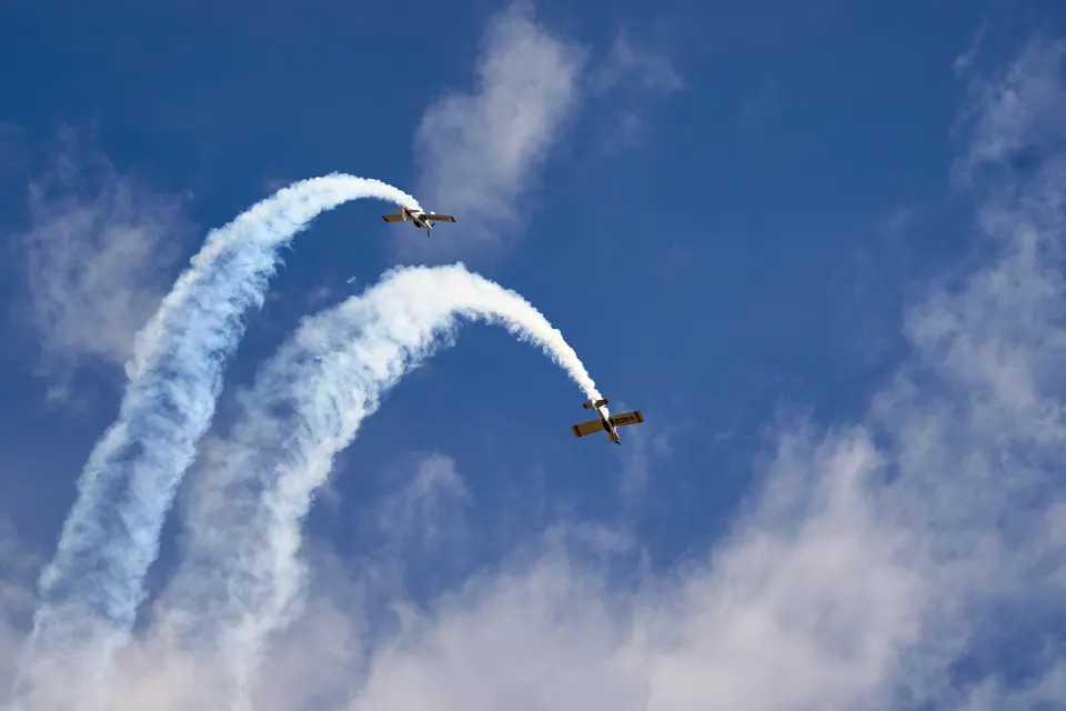 Two aircraft dive apart with curved white smoke trails against a blue sky