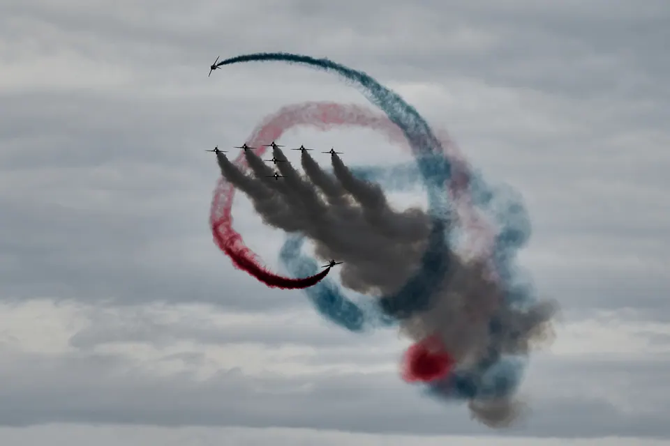 Looping red and blue smoke trails wrap around an aircraft formation