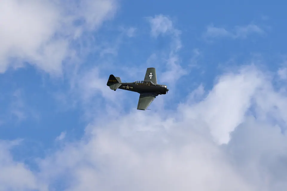 A single propeller aircraft banks against blue sky and white clouds