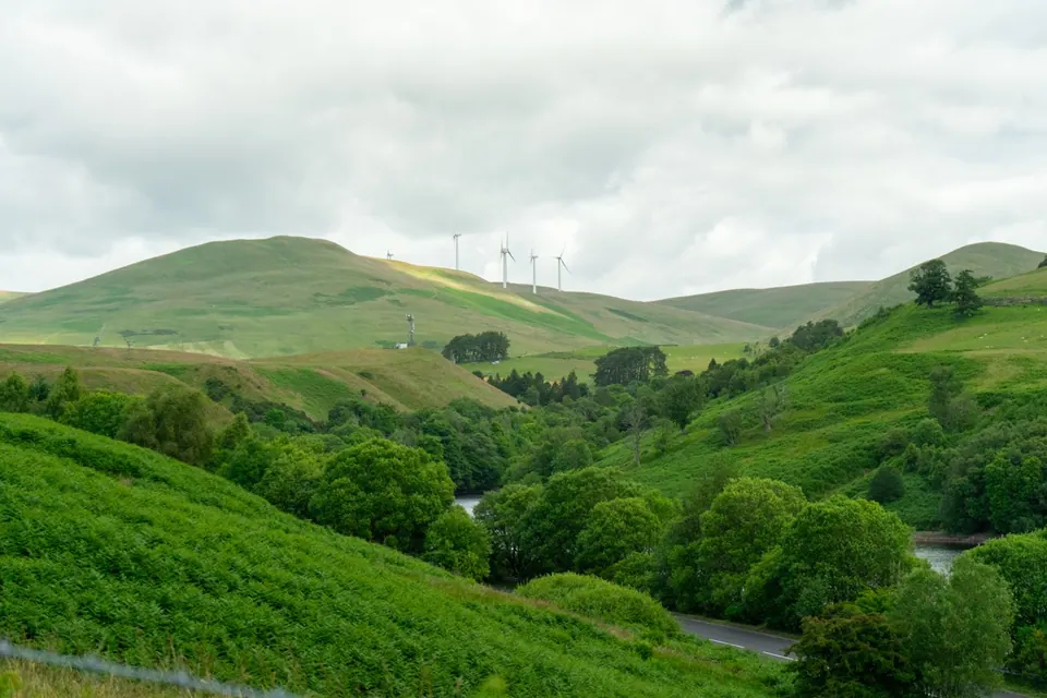 Green slopes and trees descend into a broad valley beneath overcast skies