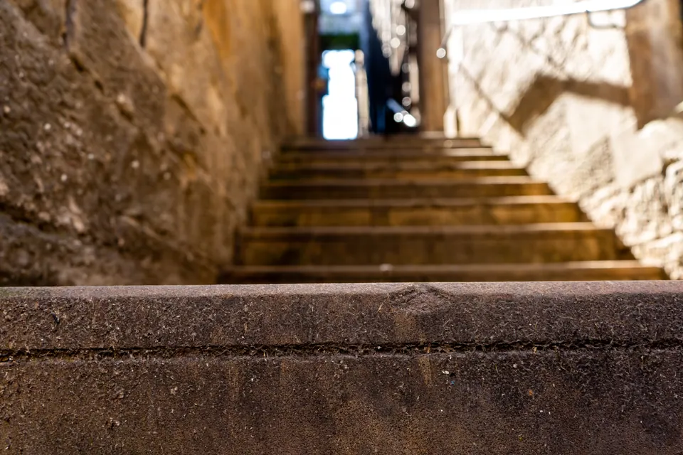 Sunlight falls across worn stone steps climbing through a narrow passage.