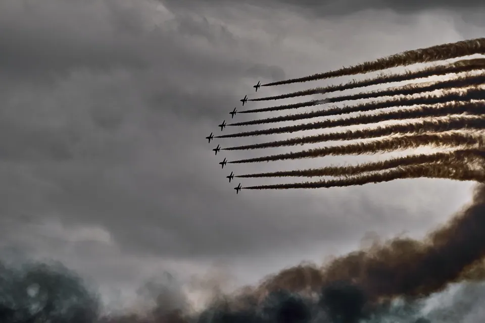 Parallel smoke trails curl behind a row of aircraft against a dark sky