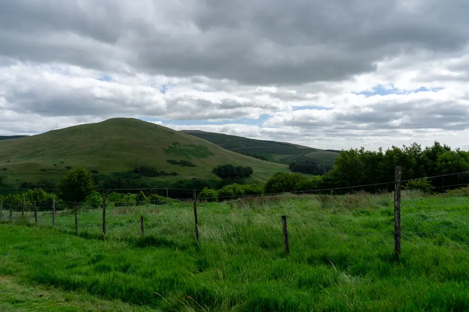 Fenced pasture and hills beneath a dark cloudy sky