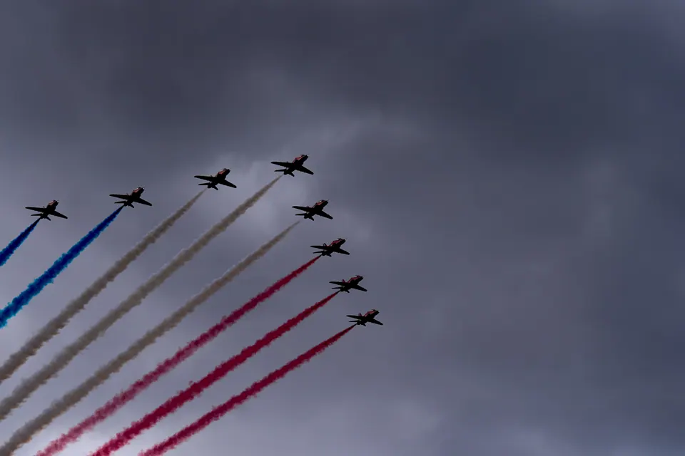 A tight formation of aircraft climbs diagonally above long coloured smoke trails
