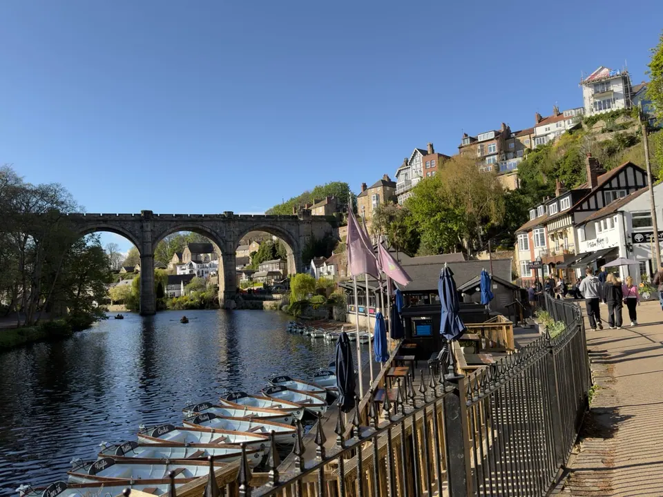 A stone railway viaduct crosses a river beside boats and hillside buildings
